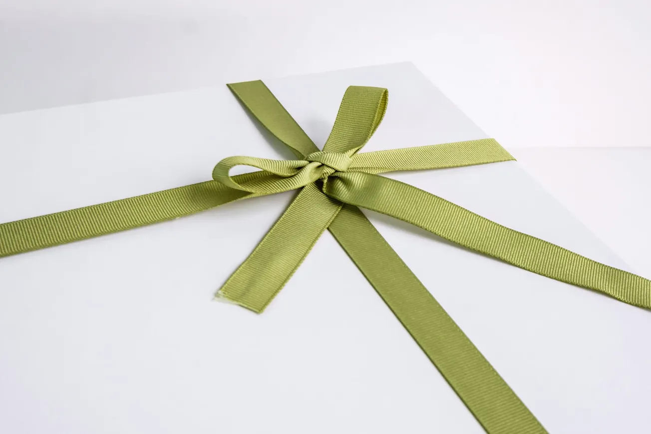 A white gift box with a neatly tied pale green ribbon bow on top, creating an elegant and inviting presentation.