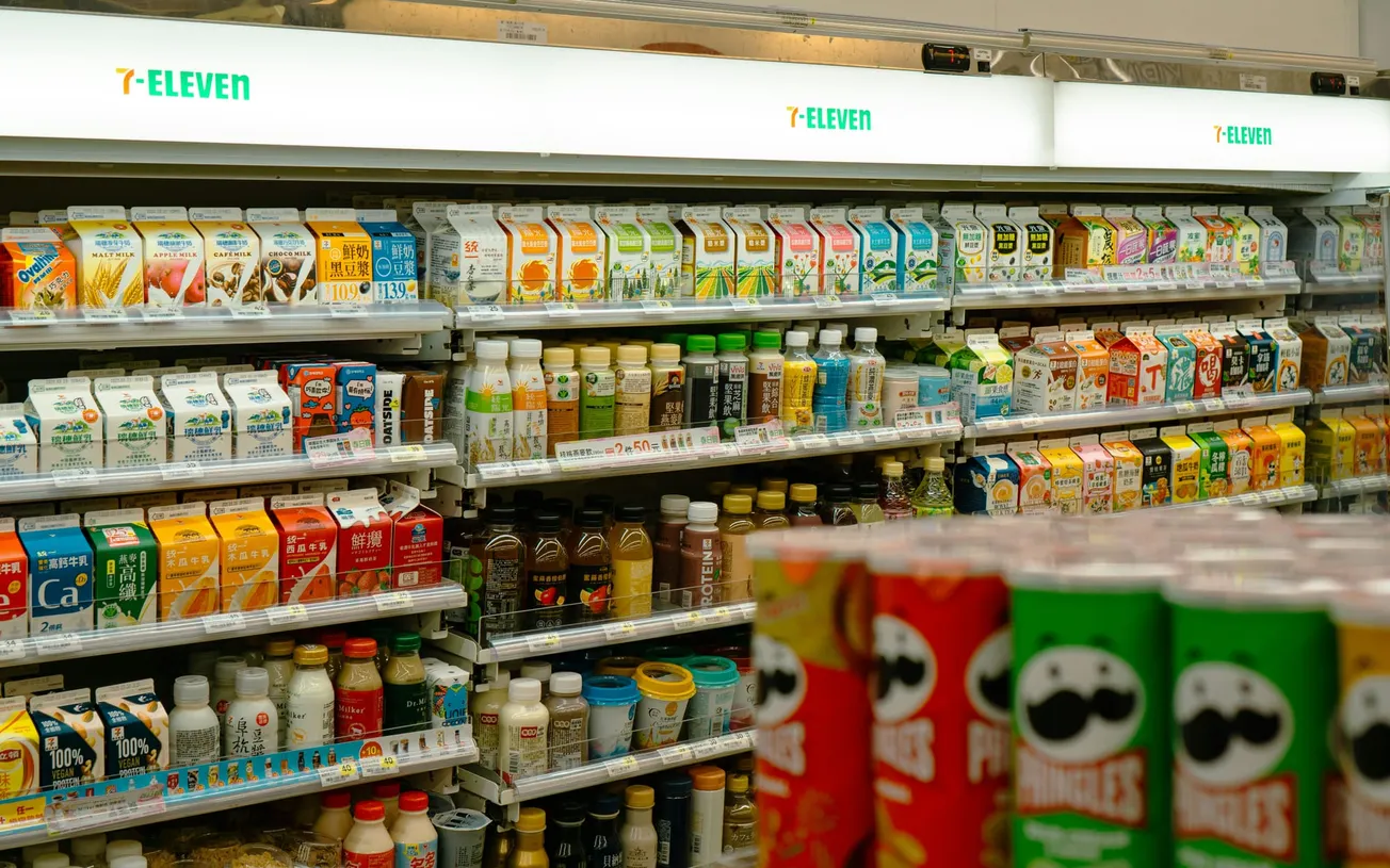 Shelves in a 7-Eleven are lined with colorful beverage cartons and bottles. The atmosphere is bright and organized, conveying convenience and variety.