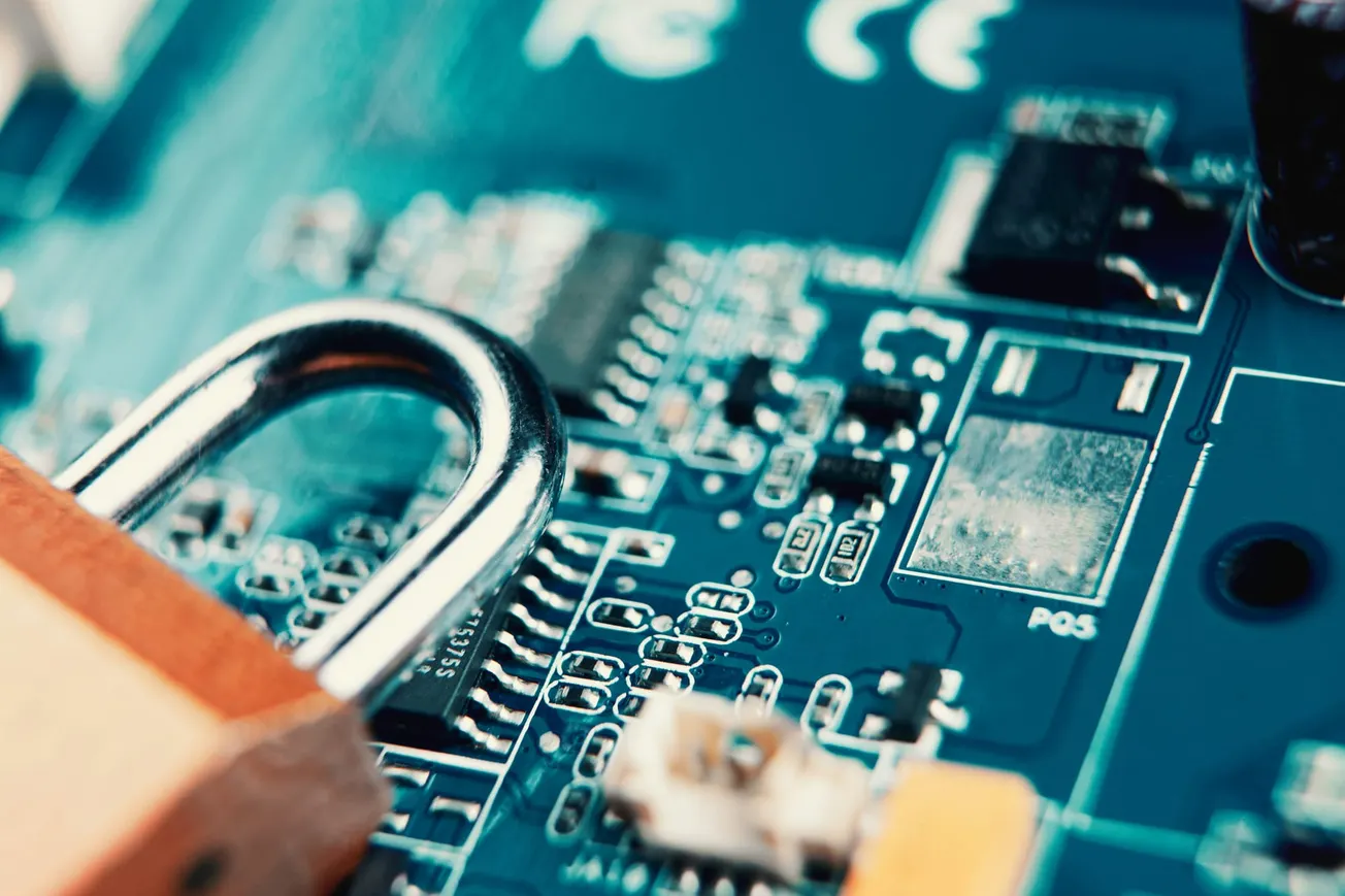Close-up of a padlock placed on a blue circuit board, symbolizing cybersecurity. The metallic lock contrasts with intricate electronic components.