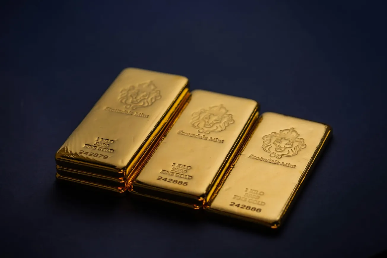 Three shiny gold bars with embossed logos and inscriptions are arranged on a deep blue background, conveying luxury and wealth.