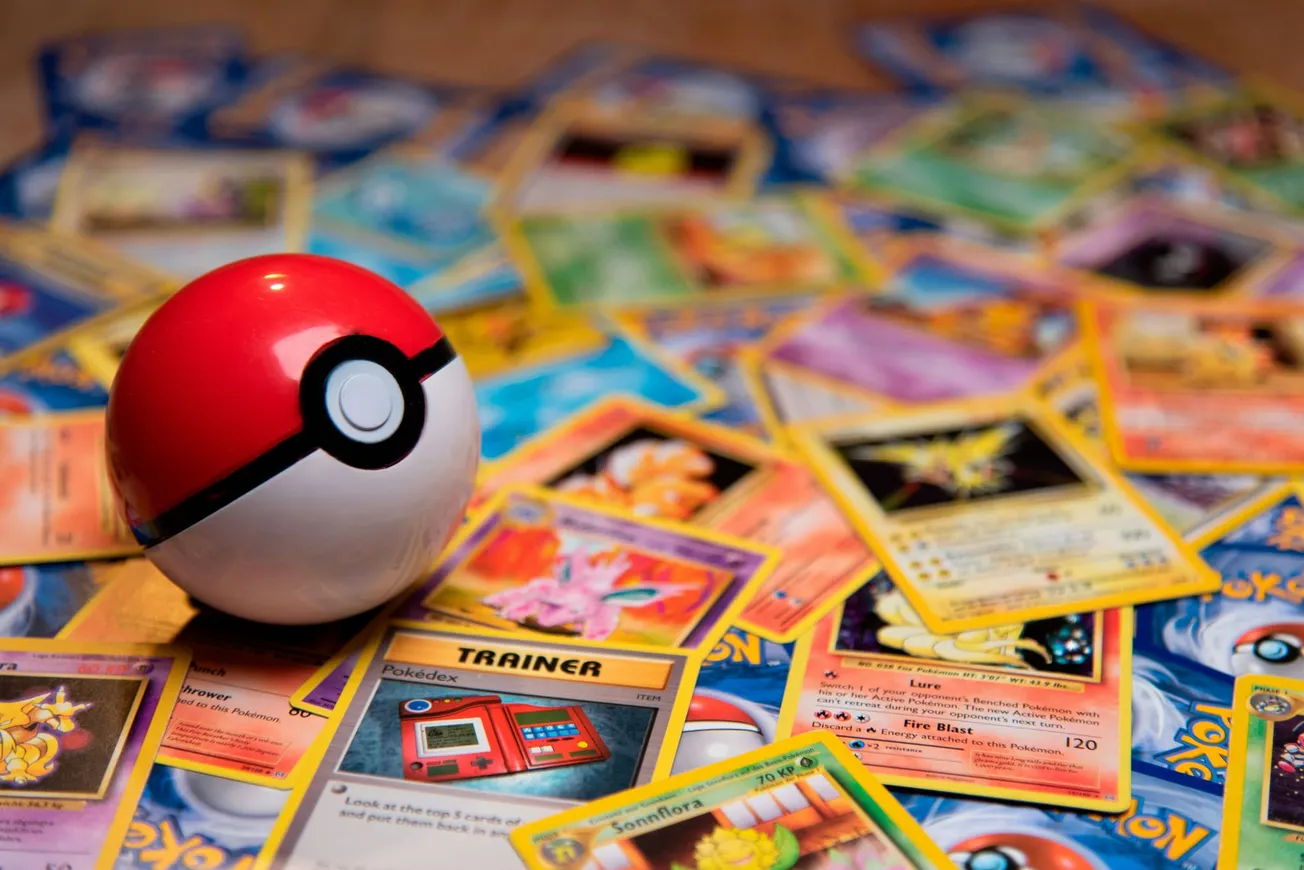 A Poké Ball sits atop a scattered collection of colorful Pokémon trading cards. The scene evokes nostalgia and excitement for the Pokémon universe.
