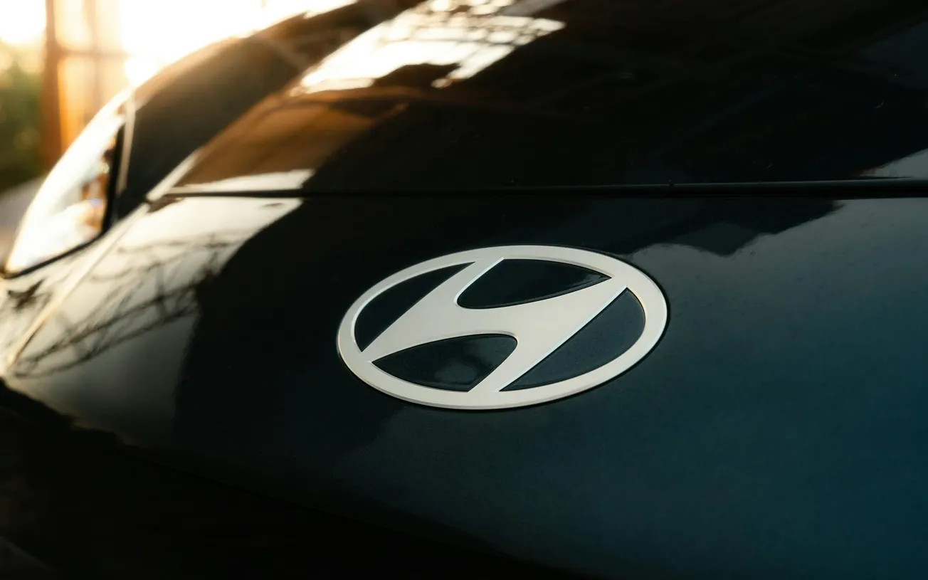 Close-up of a black car hood featuring the Hyundai logo in a softly lit setting. The lighting creates a warm ambiance with faint reflections.