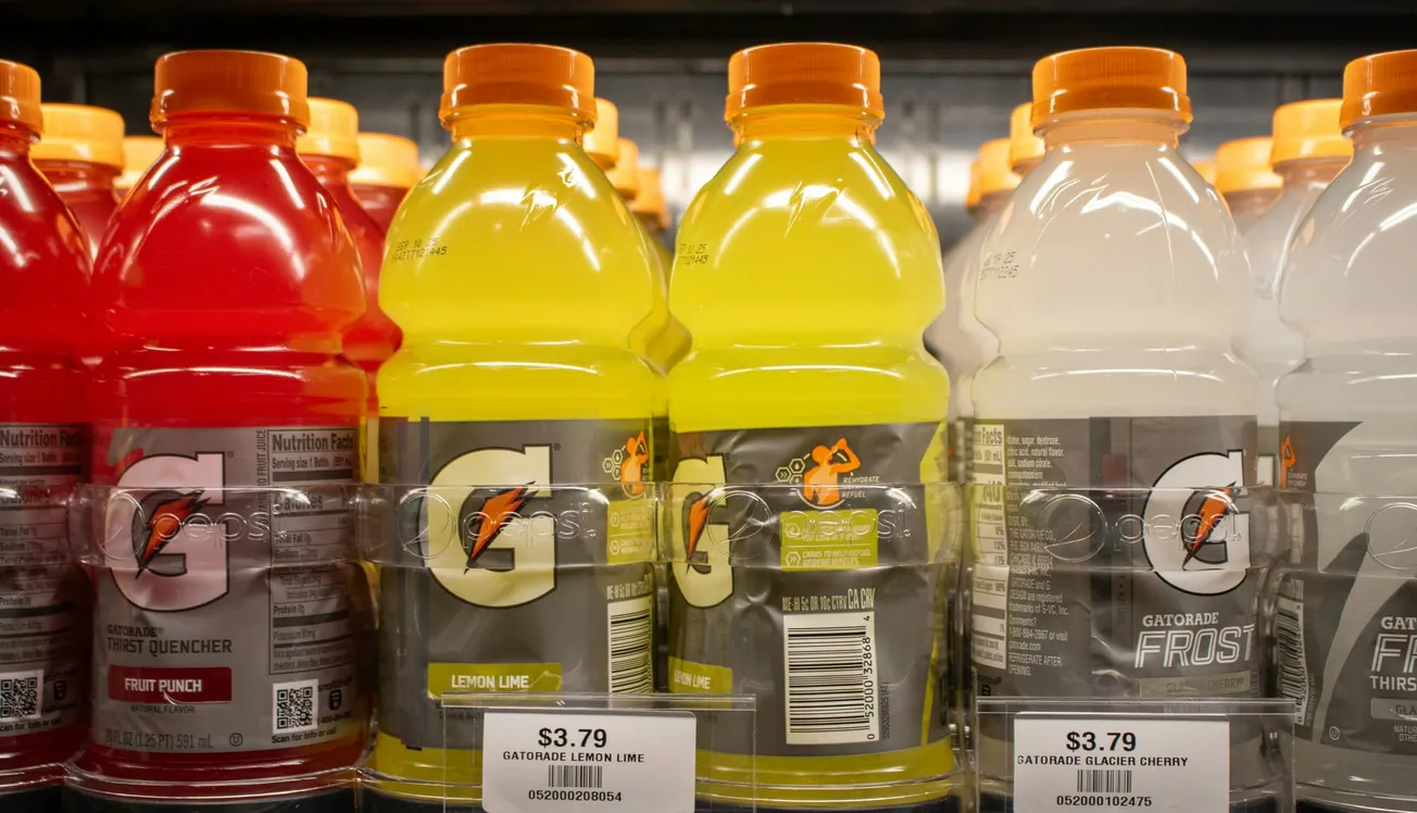 Bottles of Gatorade in red, yellow, and white on a store shelf with orange caps. Price tags below read $3.79. Energetic and bright display.