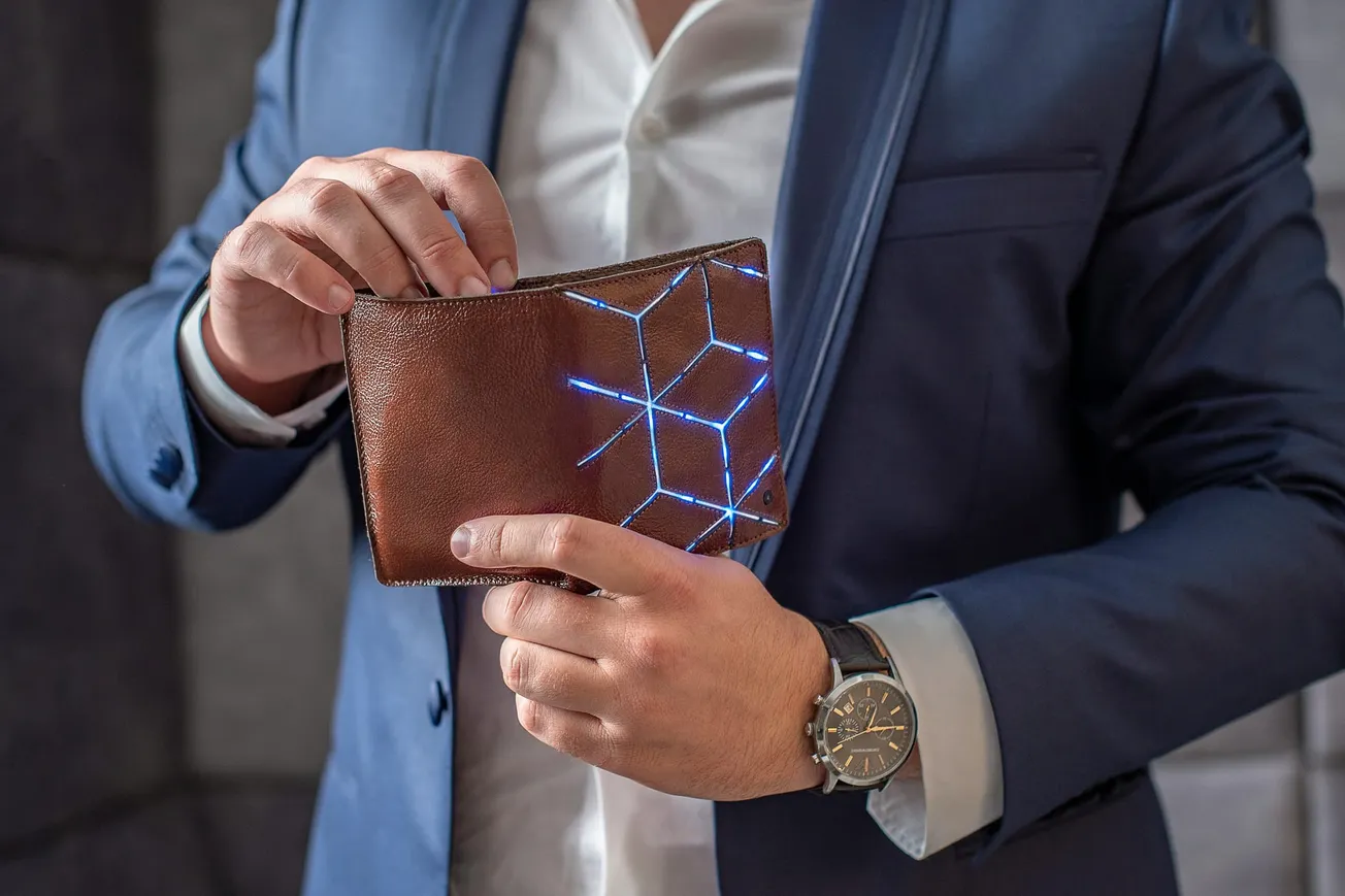 A person in a blue suit holds a brown wallet with glowing blue geometric patterns. The scene conveys a modern and stylish tone.