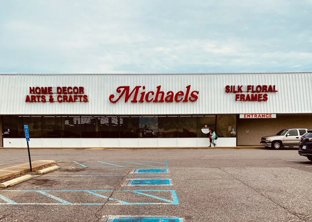 A diverse group of customers, including adults and children, joyfully personalize party decorations at a colorful DIY bar located within a Michaels retail store.