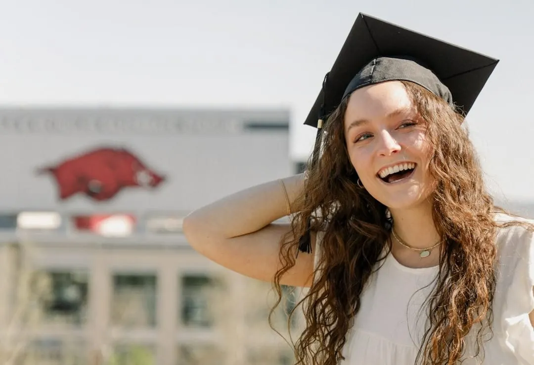 University of Arkansas graduate in a cap, standing in front of Donald W. Reynolds Stadium.