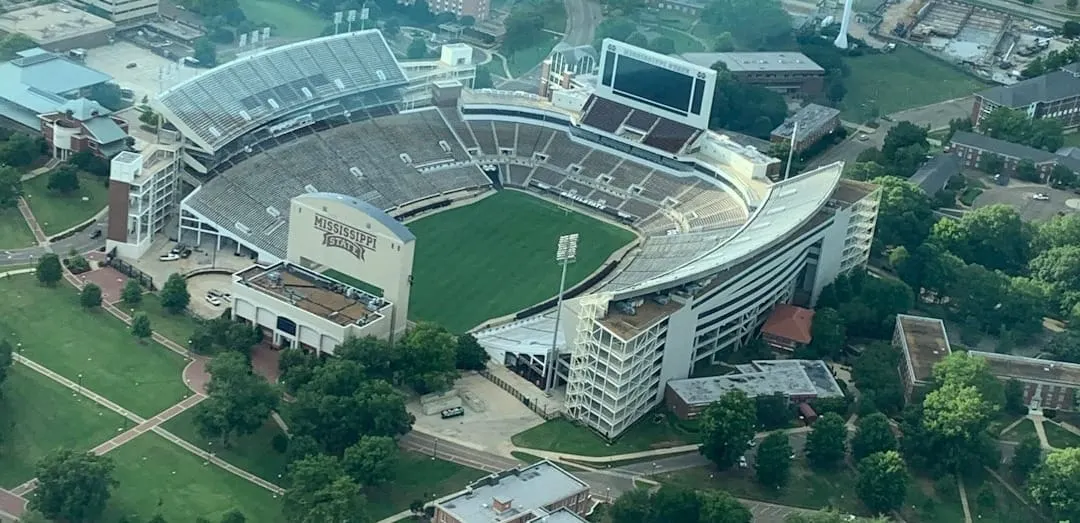 An aerial photograph captures a vibrant university sports stadium, highlighting the economic activity and community engagement in the surrounding urban area.