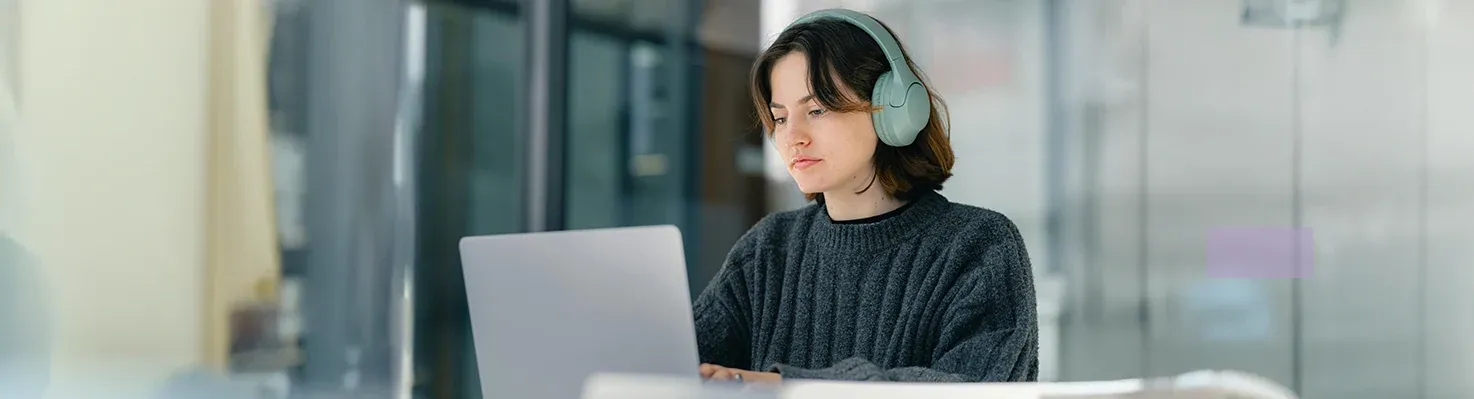 Autistic person using noise-canceling headphones while working on a laptop.
