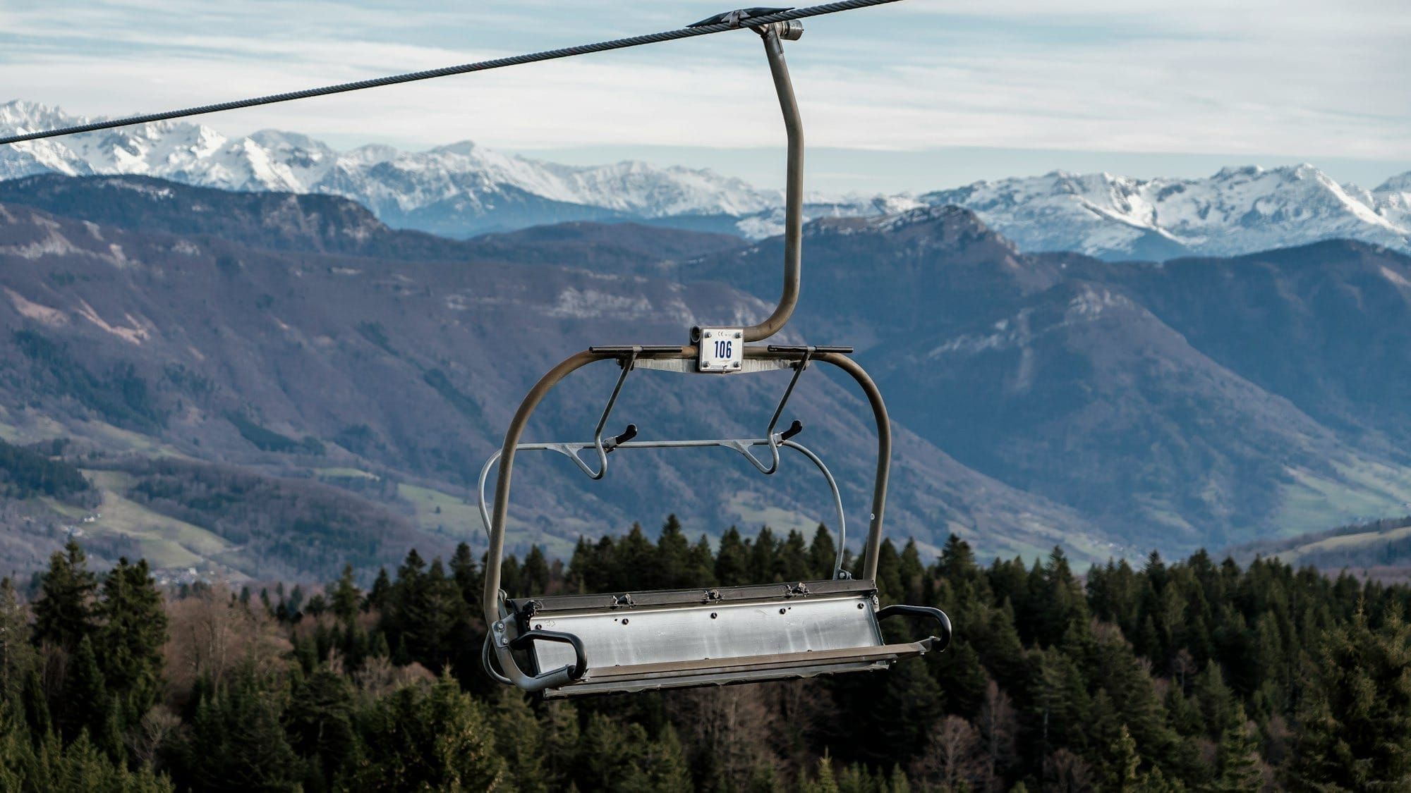 Empty chairlift with green hills below and white- capped mountains in the distance.