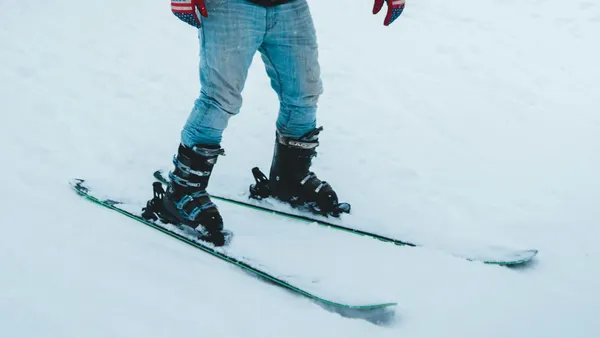 Man wears faded blue jeans while skiing on snow.