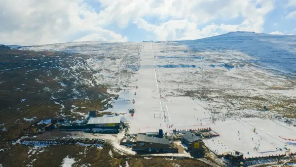 A very wide straight ski run covered in snow amidst mountains that are a mix of brown and white