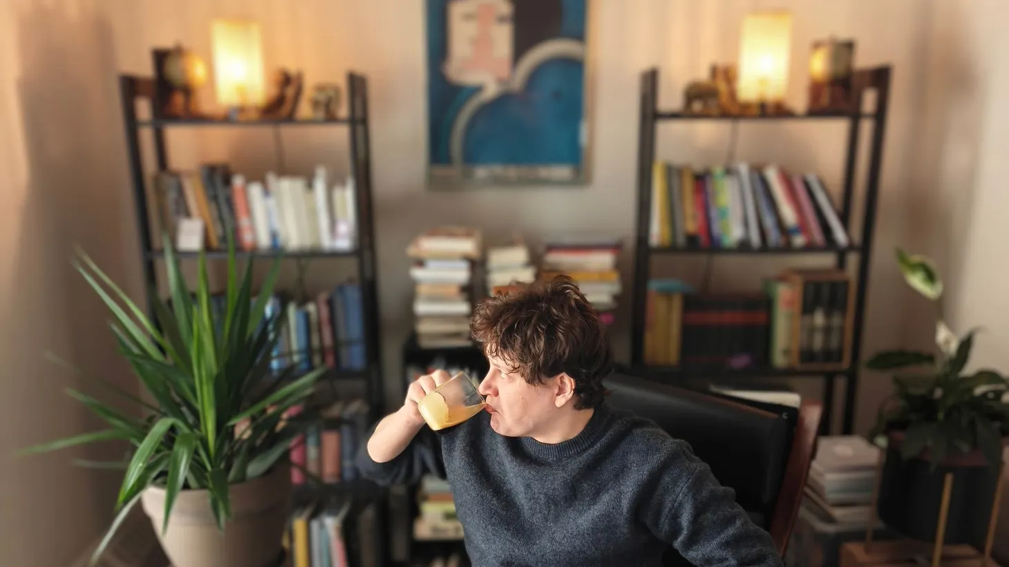 Portrait of author of Bibelotages, Jay Miller, in his personal library looking dour with a black coffee pressed to his lips looking out the window wistfully.