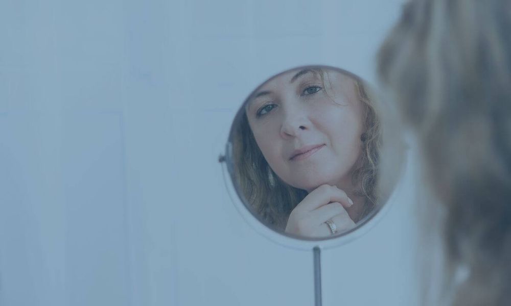 Woman suffering from anxiety looking at herself in the mirror | Article about easing anxiety with calm magnesium gummies