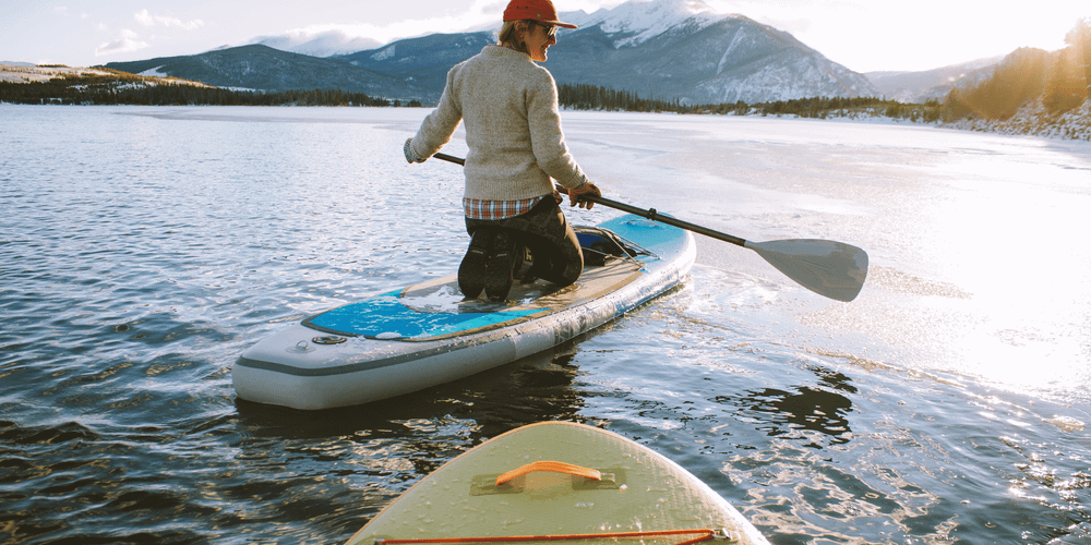 Paddle board accessories | Paddleboarder on lake with mountains in background.