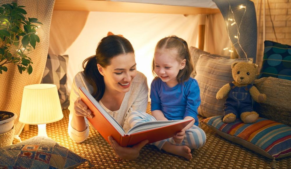 Mother reading to child in a homemade tent in the house with a rechargeable light bulb for lamps