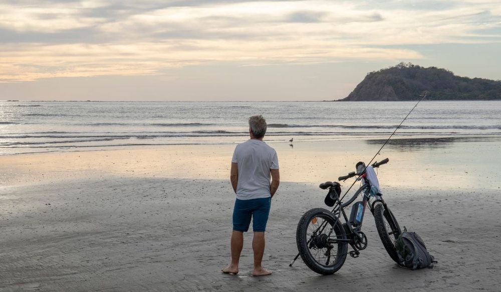 Man standing beside his ebike at the lake, with a fishing pole and backpack