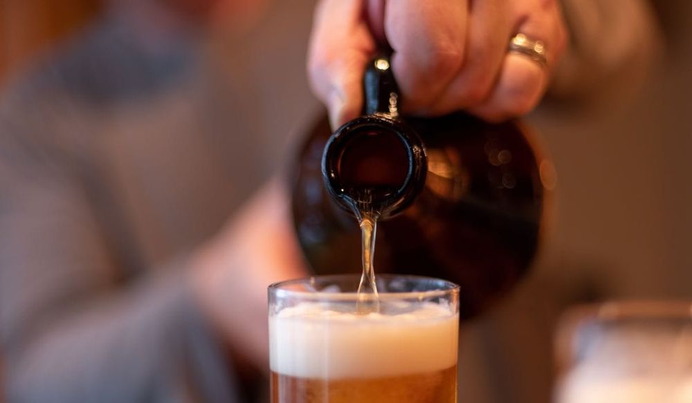 Beer Growler in dark glass pouring  beer into a glass.