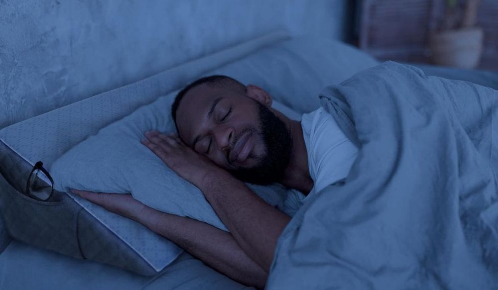 Man sleeping with headboard pillow wedge, glasses tucked securely in side pocket.