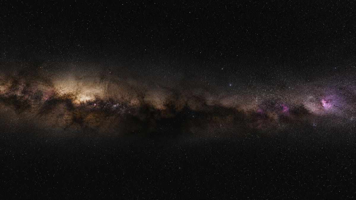 Wide-field view of the Milky Way band, its bright galactic core star cloud, dark dust lanes and pink emission nebulae across a near-black southern sky