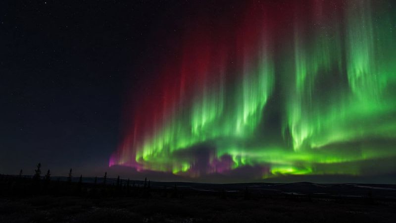 Green aurora curtains with a red crown over an arctic landscape, showing what causes the northern lights