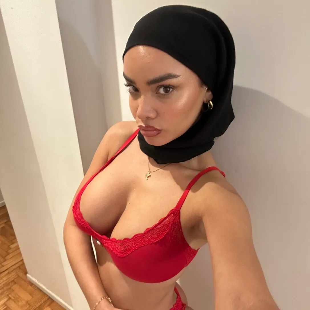 Salma Iman in a black headscarf and red lace lingerie, taking a selfie against a white wall