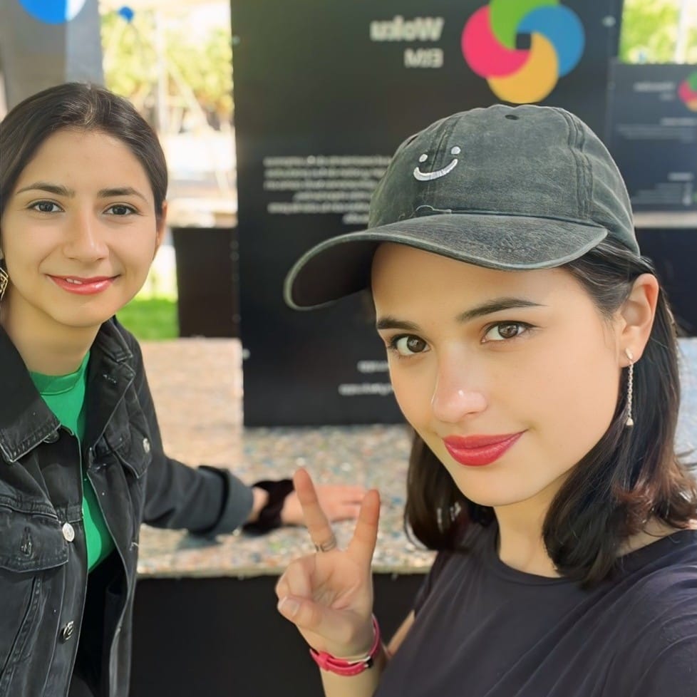 Paula Riquelme y Sofía en el stand de woku en el ETMday 2023, posando con gestos de victoria frente a un cartel informativo de woku.