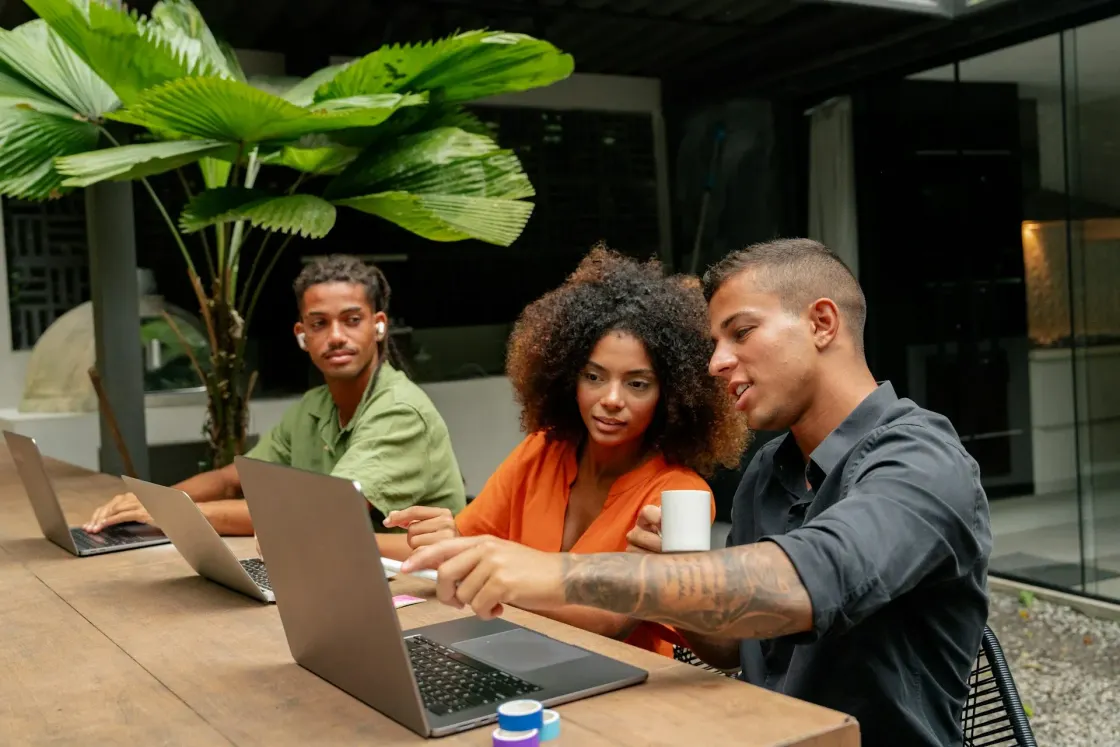 Small team collaborating on laptops in an open-air workspace, representing a hybrid work team planning cadence, core hours, and outcome-based metrics.