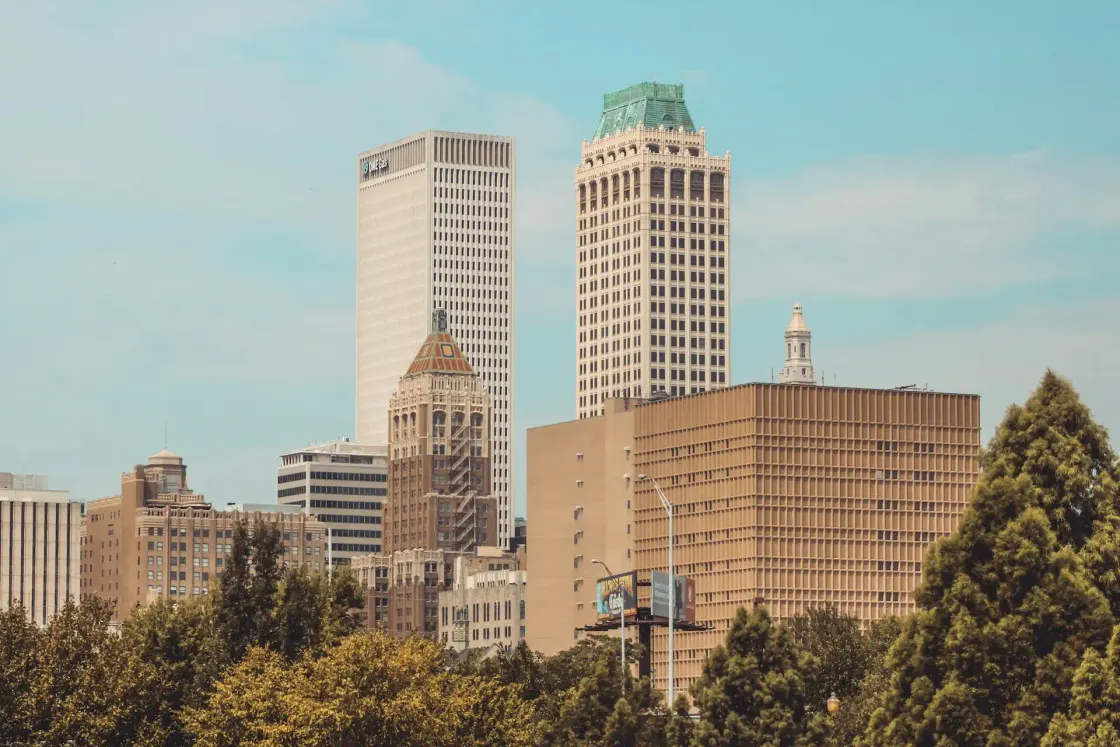 Downtown Tulsa, Oklahoma skyline with office towers rising above trees on a clear day.
