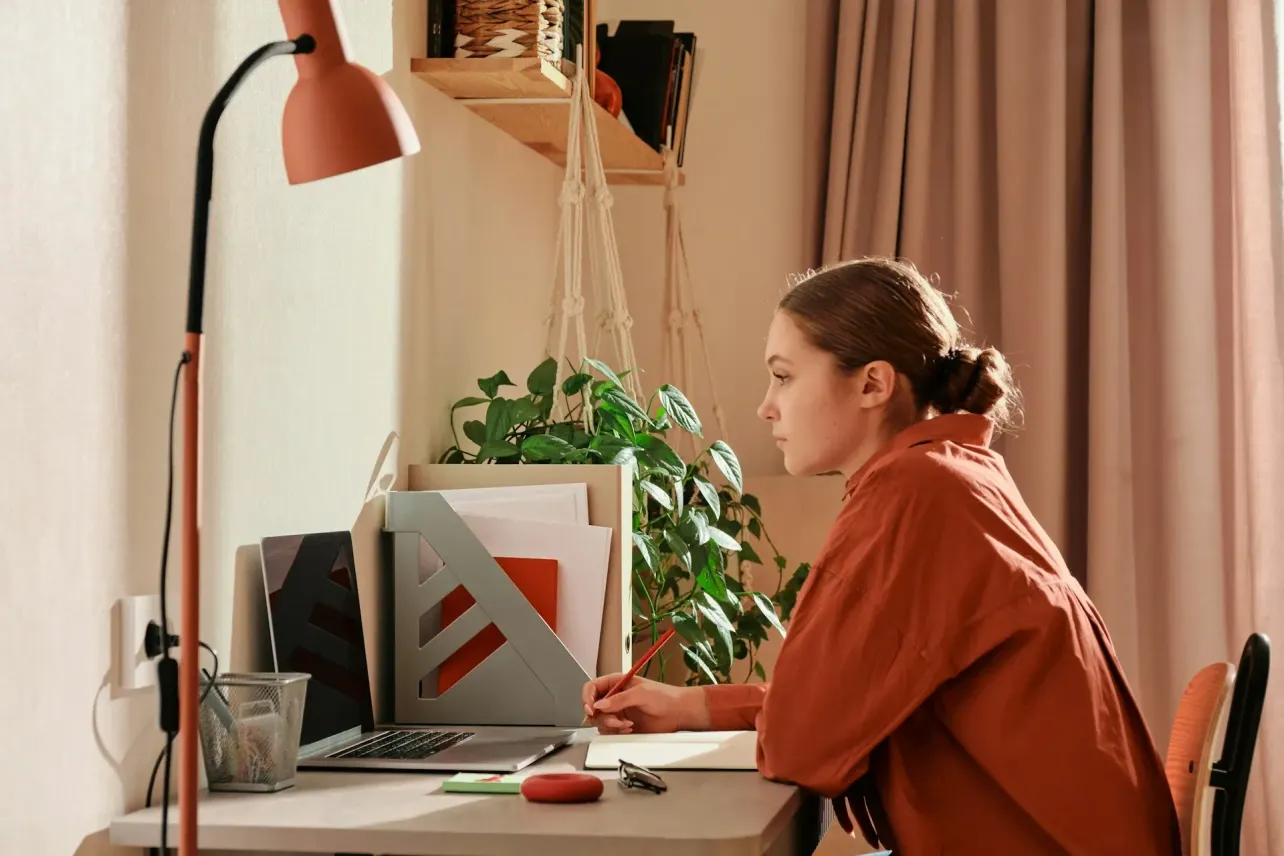 Person in a warm home office writing in a notebook beside an open laptop, representing an async written standup update.