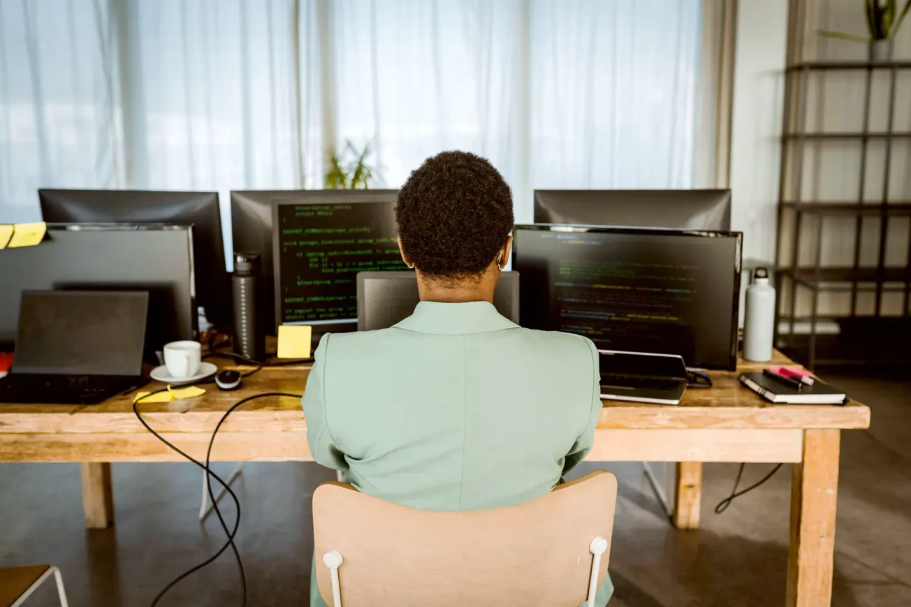 Ein Mann sitzt am Schreibtisch und blickt auf mehrere Bildschirme. Credit: IMAGO/MASKOT