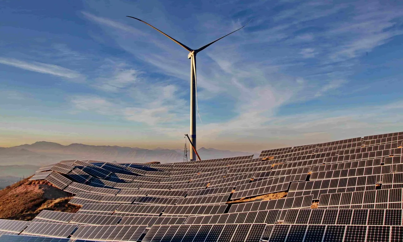 Solaranlagen und Windkraftanlage vor hügeligem Hintergrund. Credit: IMAGO/Xinhua