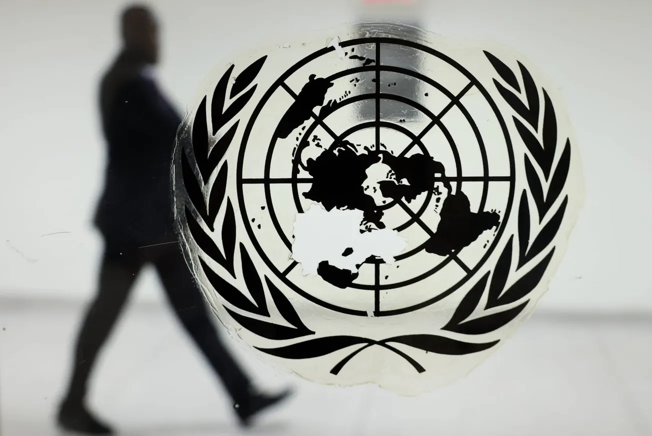 Logo der UN im Vordergrund auf einer Scheibe, im Hintergrund läuft ein Mann (Symbolbild). Credit: IMAGO/ITAR-TASS