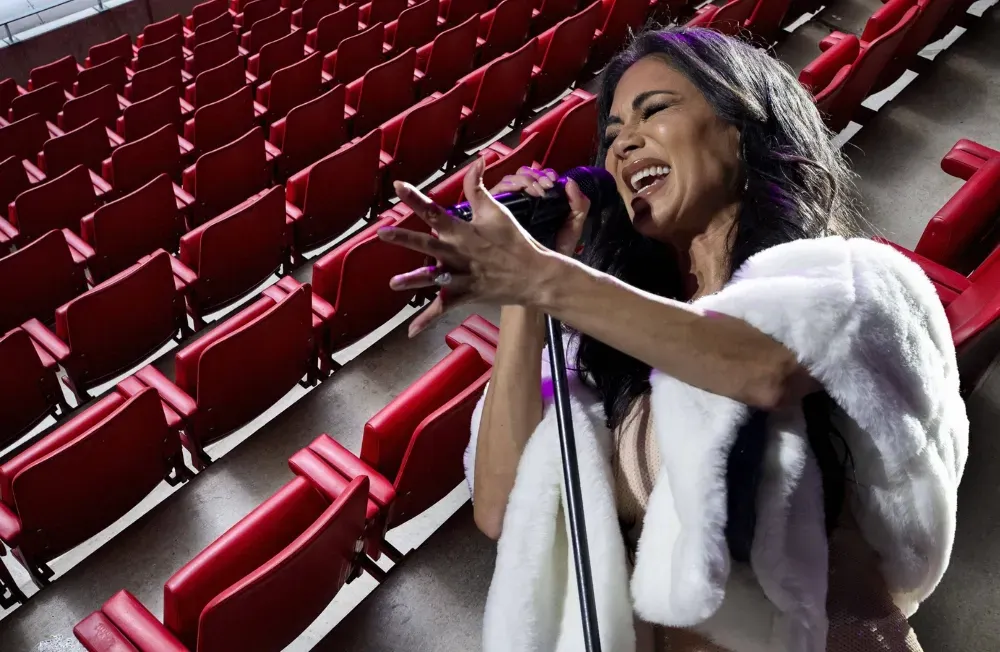 Nicole Scherzinger im Vordergrund singend, im Hintergrund leere Sitze in einer Konzerthalle. Collage: Surplus, Material: IMAGO/Vitalii Kliuiev/Cover-Images