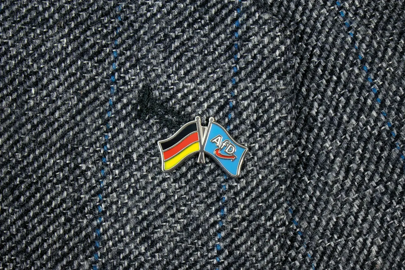 Brosche mit Deutschland- und AfD-Fahne auf grauem Sakko. Credit: IMAGO/Steinach