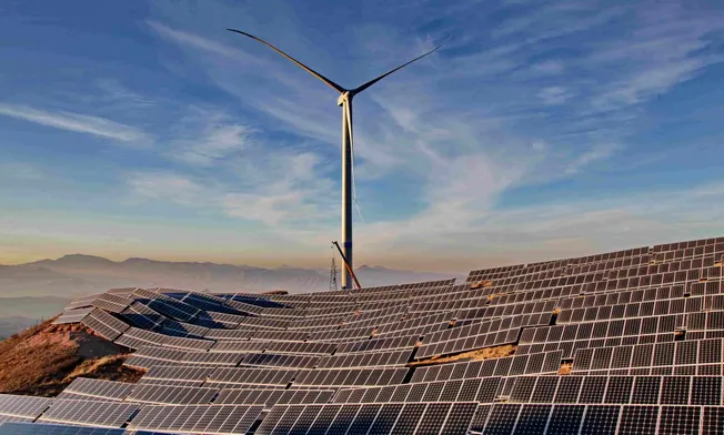 Solaranlagen und Windkraftanlage vor hügeligem Hintergrund. Credit: IMAGO/Xinhua