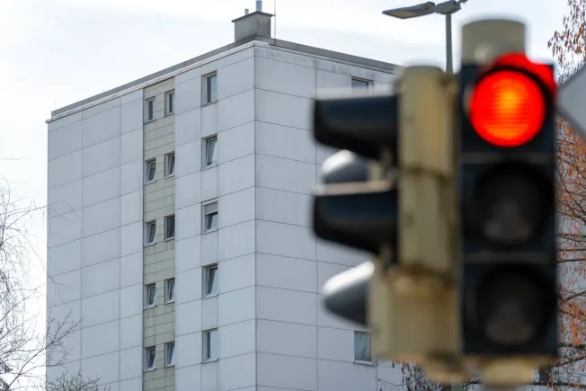 Ein Häuserblock im Hintergrund, im Vordergrund eine Ampel, die rot anzeigt. Credit: IMAGO/Bihlmayerfotografie