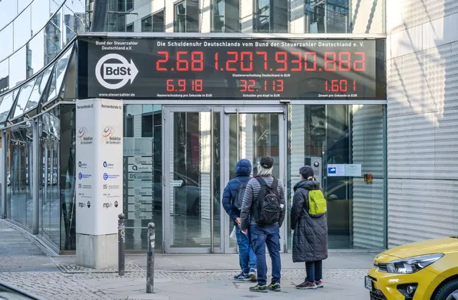 Passanten beobachten die Schuldenuhr des Bunds der Steuerzahler e.V. in Berlin (Symbolbild). Credit: IMAGO/Joko