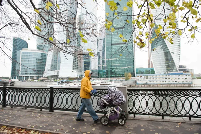 Vater schiebt einen Kinderwagen, im Hintergrund Hochhäuser aus Glas. Credit: IMAGO/Dreamstime.