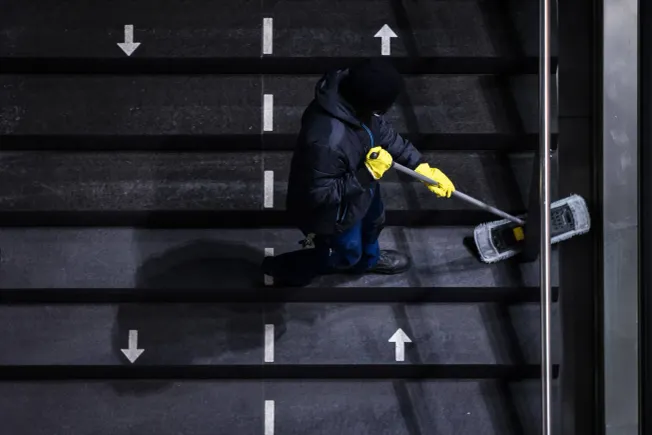 Eine Reinigungskraft wischt eine Treppe, die mit Pfeilen fuer die jeweiligen Laufrichtungen markiert ist. Credit: IMAGO/photothek