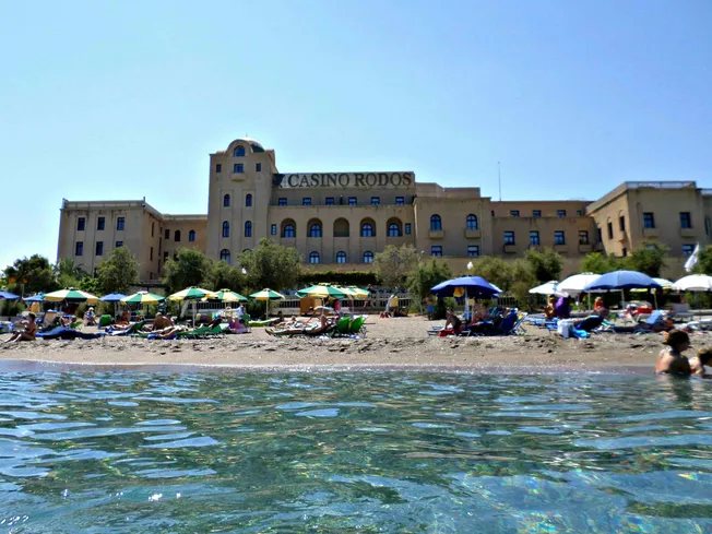 Strand mit Sonnenschirmen vor dem »Casino Rodos« auf Rhodos (Griechenland). Credit: IMAGO/Dreamstime.