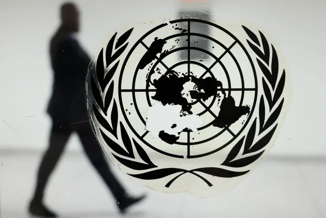 Logo der UN im Vordergrund auf einer Scheibe, im Hintergrund läuft ein Mann (Symbolbild). Credit: IMAGO/ITAR-TASS