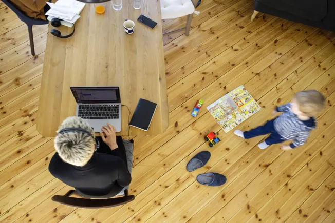 Eine Frau sitzt am Esstisch und arbeitet im Homeoffice, neben ihr spielt ein Kind (Symbolbild). Credit: IMAGO/photothek
