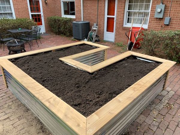 A U-shaped raised garden bed, filled with dirt, made from cedar and corrugated aluminum roofing material for the sides.
