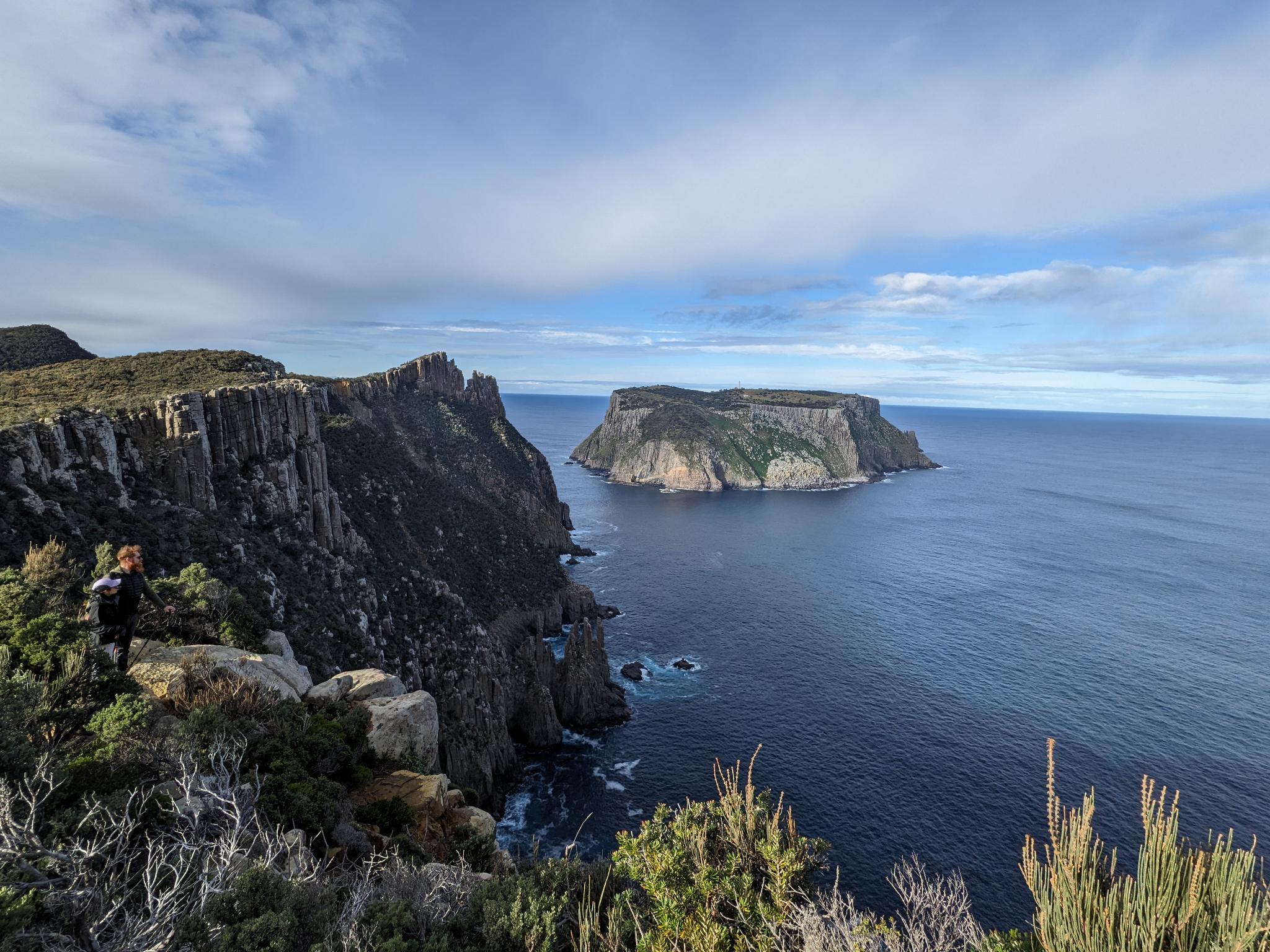 Two hikers standing upon a cliff looking out to an island in the sea, sky