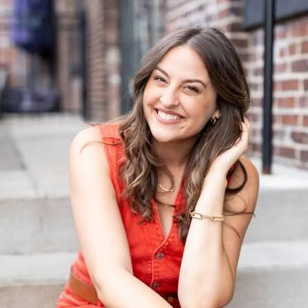 Portrait of Allea Grummert, founder of Duett, smiling while seated on outdoor brick steps wearing a sleeveless red top.