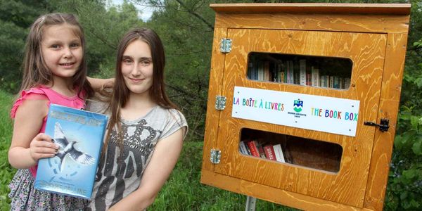 Jessyka-Meghan et Sarah-Jane, en visite au parc, devant l'une des nouvelles boîtes à livres de Morin-Heights.