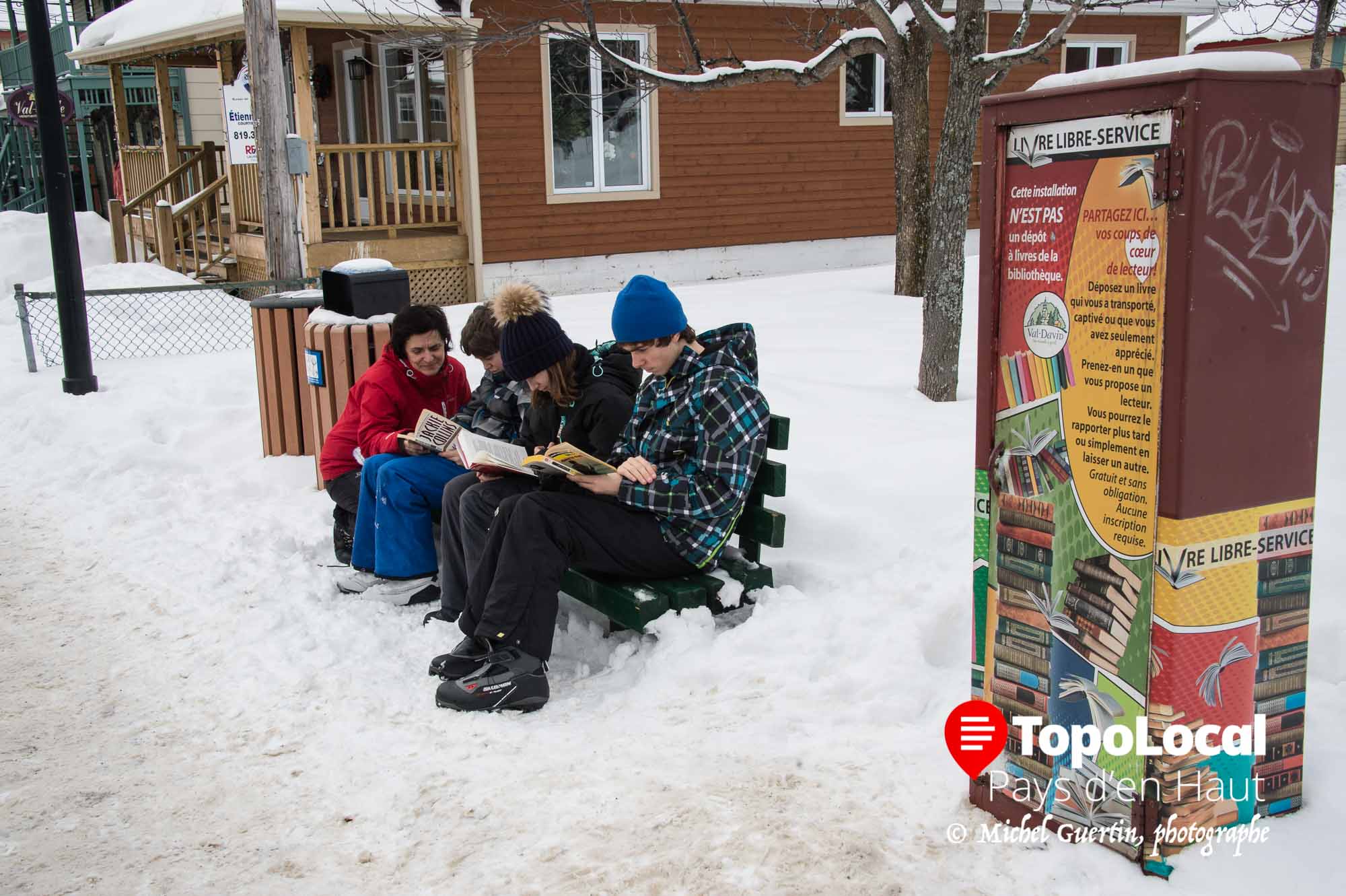 Ces jeunes en compagnie de leur mère prennent du temps pour lire un des livres mis à leur disposition gratuitement en accès libre sur la rue de l'Église à Val-David.