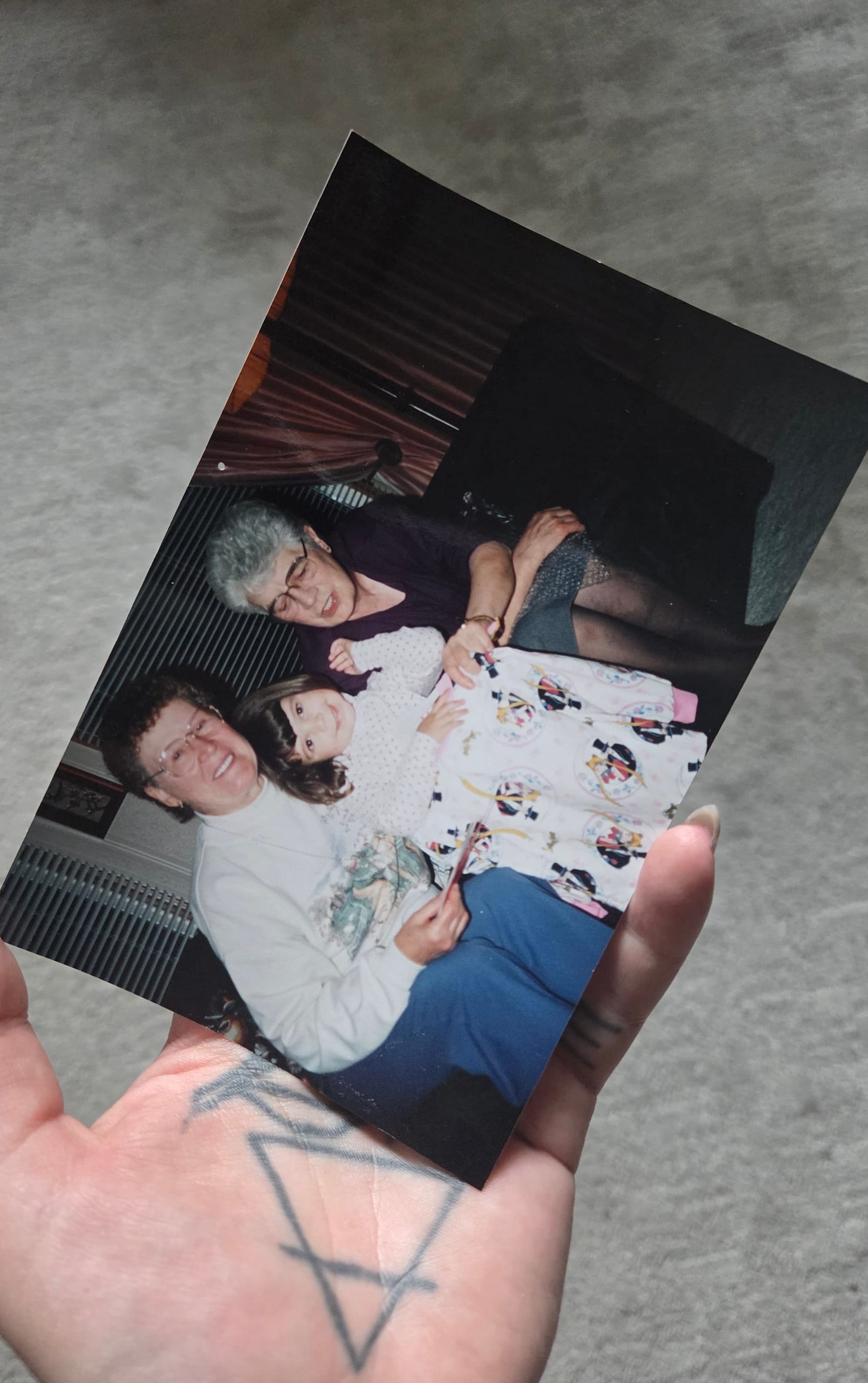 a close up of a film photo, a young girl, probably 5, with brown hair smiles while holding Sailor Moon pyjamas. Her grand mothers sit on either side of her 