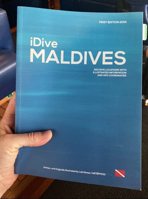 A hand holding the iDive Maldives guidebook, first edition 2015, listing 300 dive locations