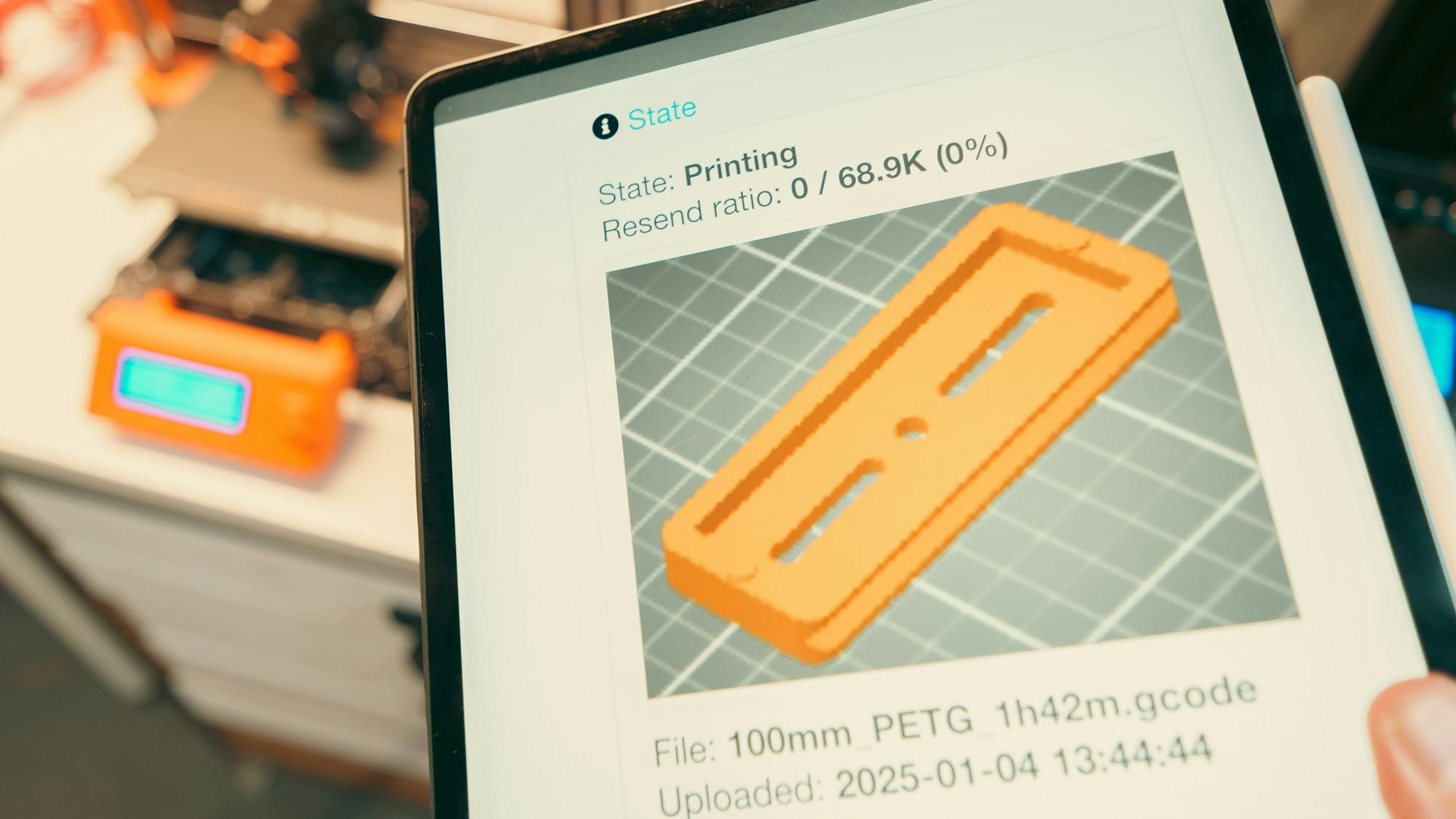 Tablet displaying 3D print progress with printer in background.